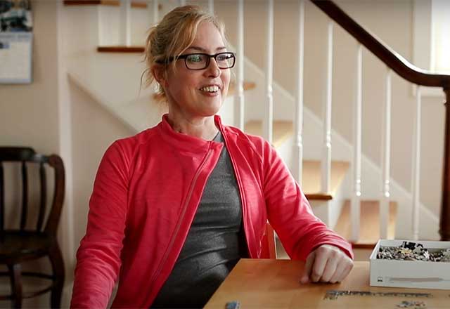 A smiling woman sits at a table in a house