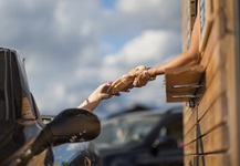 Female fast food worker handing female driver food at drive thru