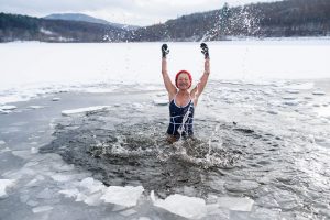 A front view of active senior woman in swimsuit splashing water outdoors in winter, cold therapy .