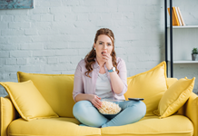 A woman sits on the couch, eating popcorn.